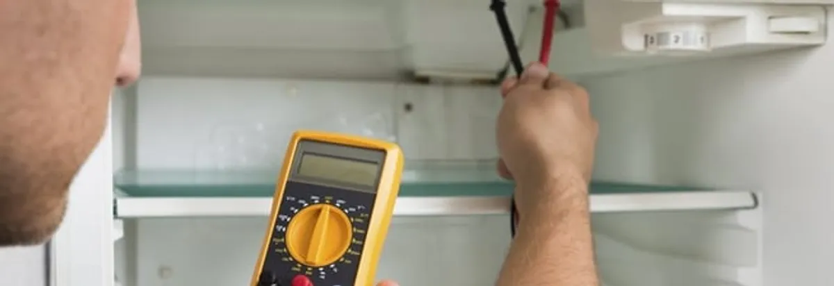 Refrigerator repair technician testing electrical components with a multimeter in Albany, NY